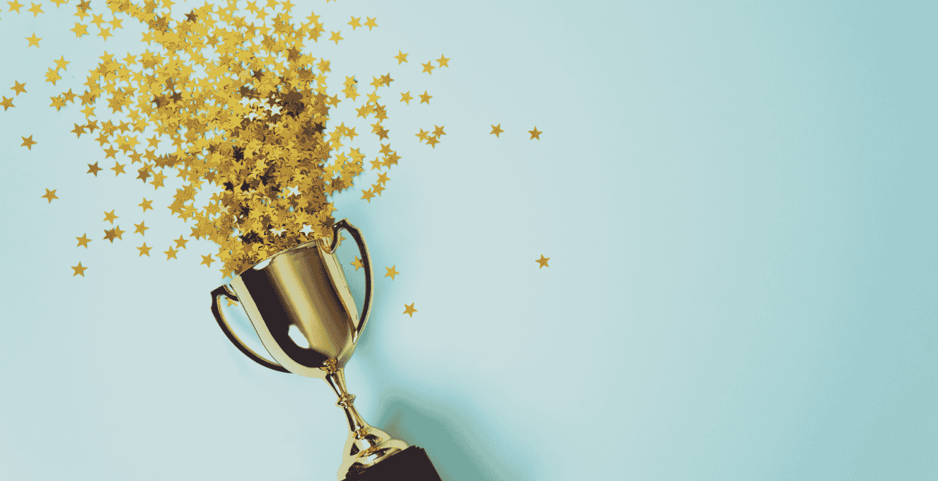 A flat lay of a trophy lying on a light blue background with confetti gold stars pouring out of it