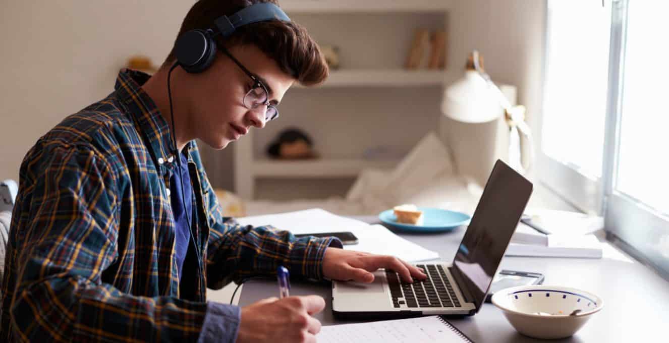 A male student sat at his desk with headphones on, in front of his laptop revising for his exams