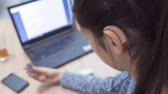 Image of a female student looking at computer wearing a hearing aid.