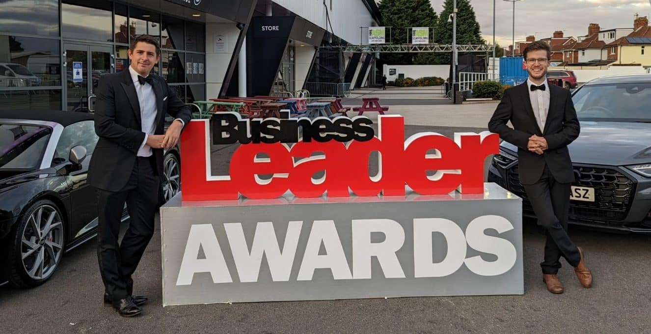 A photo of Chris and Tom standing next to a very large Business Leader Awards sign dressed in black tie