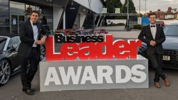 A photo of Chris and Tom standing next to a very large Business Leader Awards sign dressed in black tie