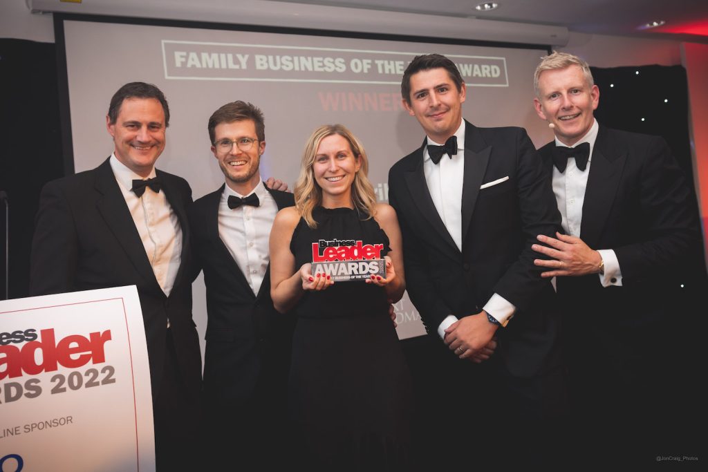 Some of the CareScribe team accepting the Family Business of the Year award at Ashton Gate. There is a woman in the centre of the image holding the award and two men either side all smiling at the camera. They are all dressed in black tie.