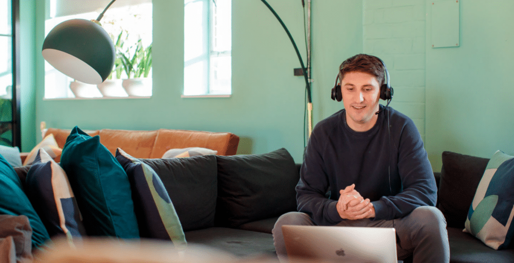 A photo of Rich who is sitting down with his laptop and wearing a headset, smiling.